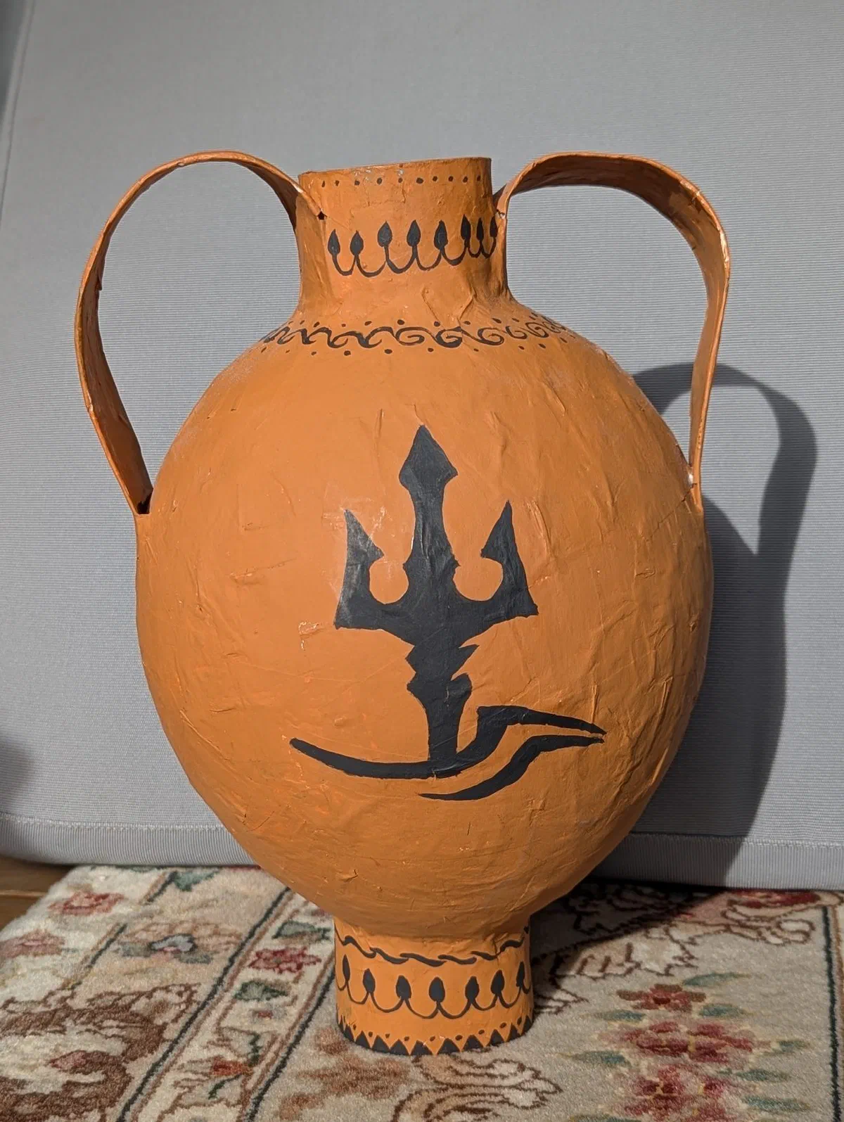 A student-made paper-mâché Greek amphora with a trident design.