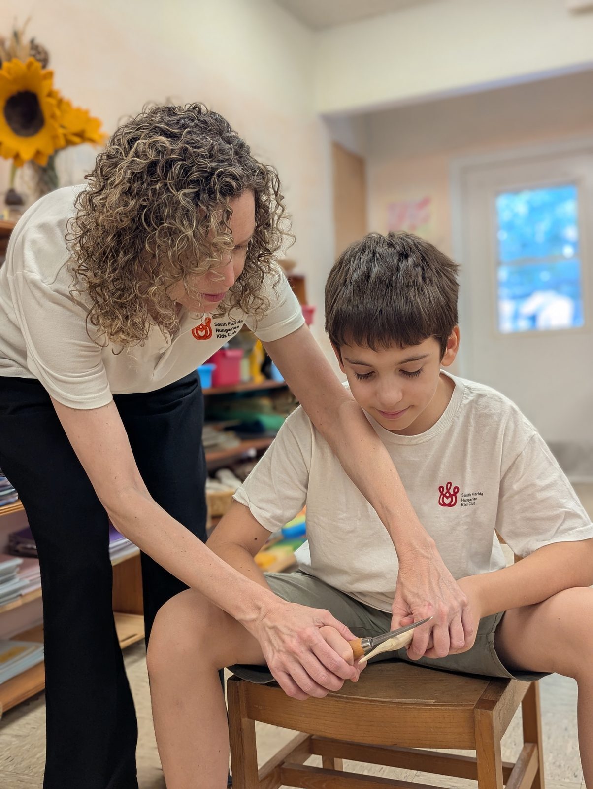 Olga guiding a young student through a careful hand-work project in the classroom.