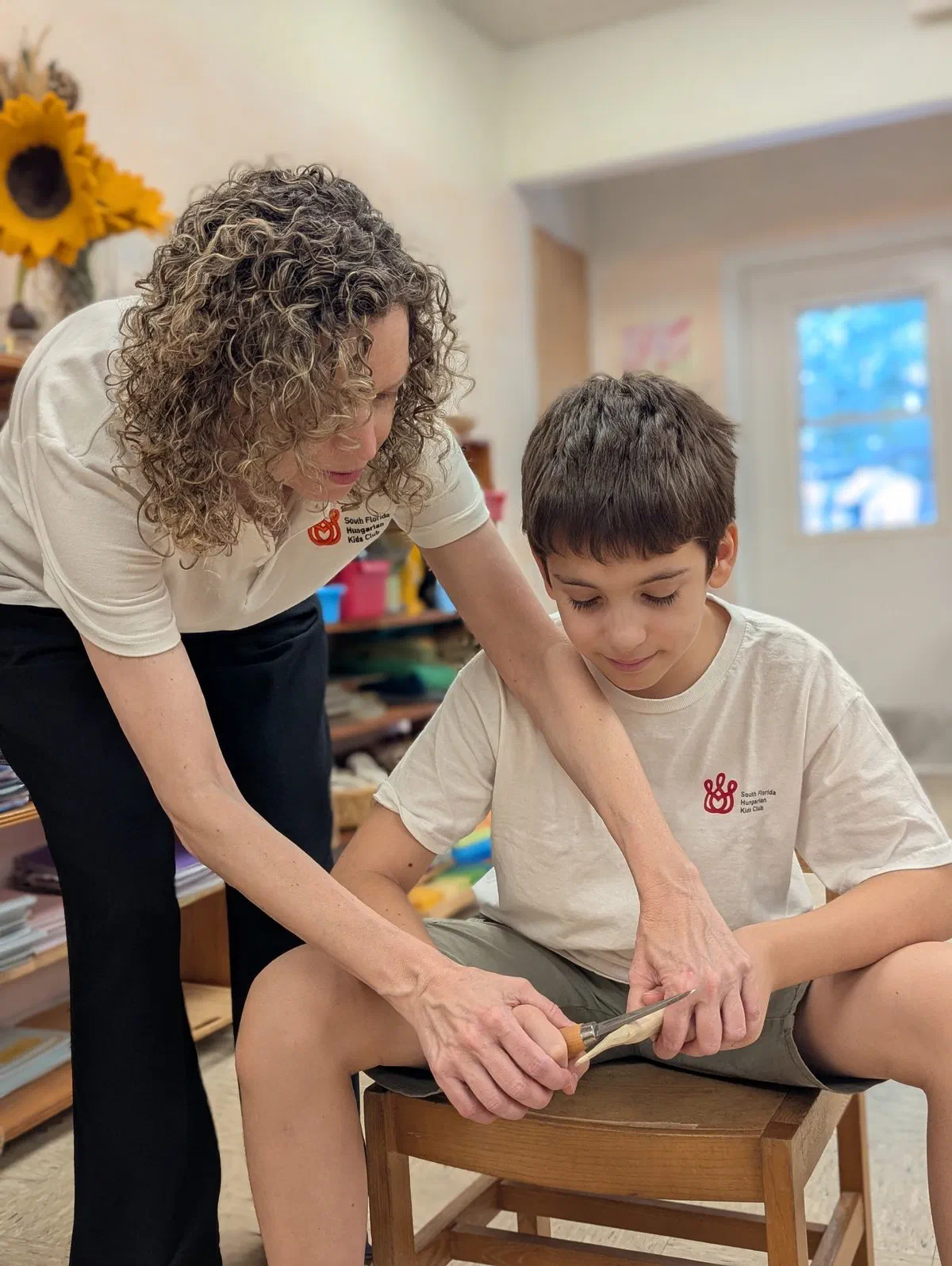 Olga guiding a young student through a careful hand-work project in the classroom.